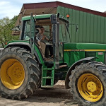 Tracteur jaune et vert avec jeune au volant, ferme