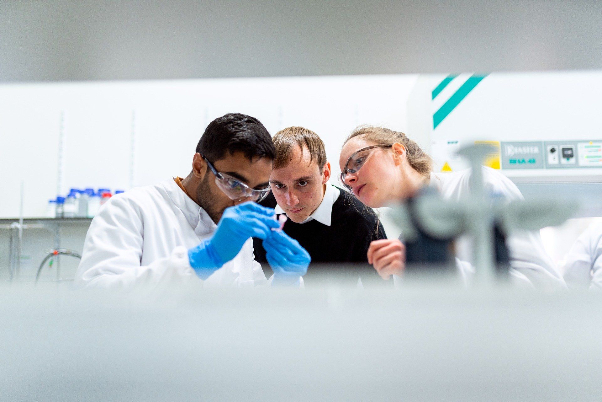 Trois ingénieurs dans laboratoire regardent un échantillon, gants bleus