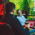 Deux jeunes assis discutent dans bureau, plantes vertes, ordinateur